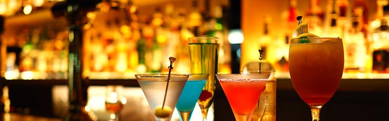 Image of glasses filled with various coloured cocktails lined up on a bar counter